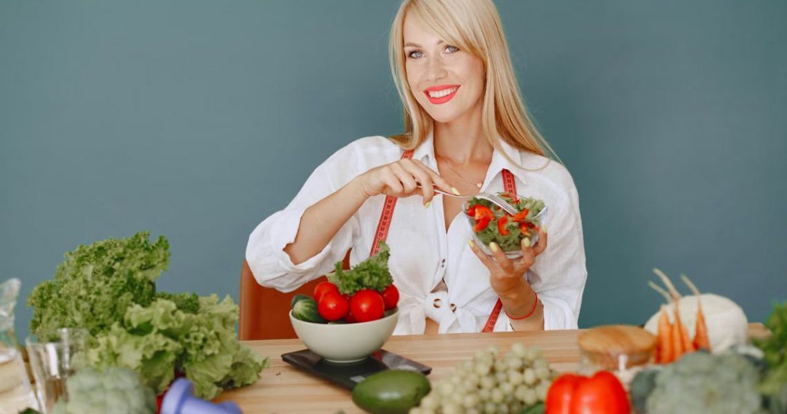 Blonde woman enjoying a fresh salad surrounded by vegetables, promoting healthy eating.