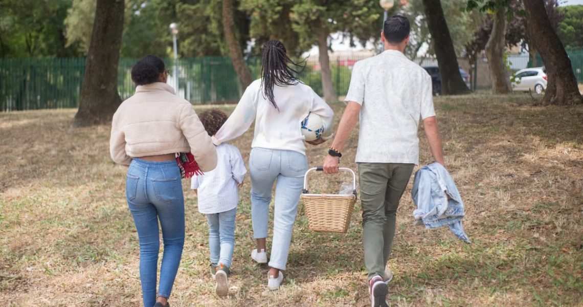 Family walking together carrying picnic basket in a sunny park.
